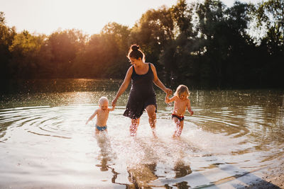 Mother and young children walking out of lake holding hands smiling