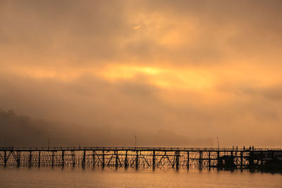 Silhouette pier over sea against sky during sunset