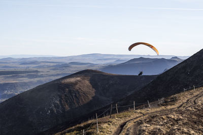 Person paragliding over landscape against sky