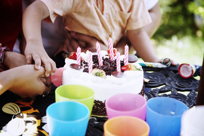 Midsection of family cutting birthday cake on table in yard