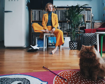 Woman sitting on chair while cat on floor at home