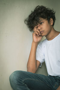 Young man looking away while sitting against wall