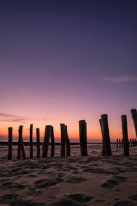 Silhouette wooden posts on beach against sky during sunset