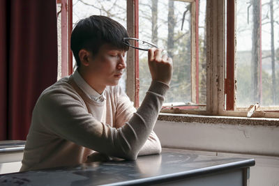 Boy looking through window while sitting on table