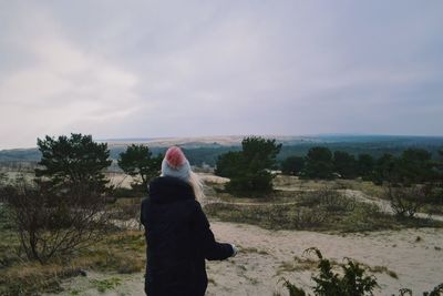 Rear view of woman standing on landscape against cloudy sky