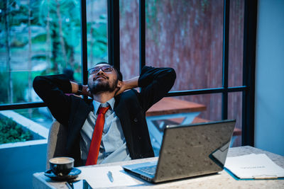 Man with hands behind head day dreaming at office