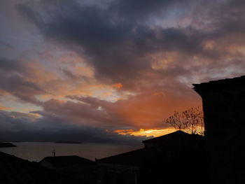 Silhouette buildings against dramatic sky during sunset