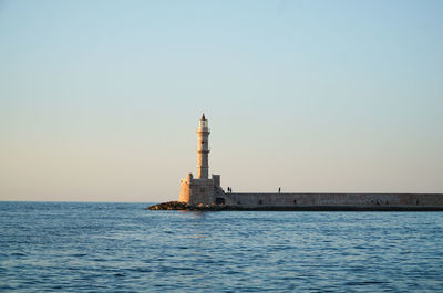 Lighthouse by sea against clear sky