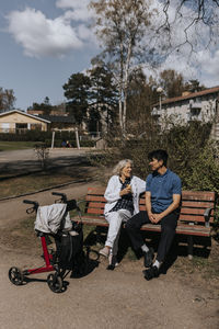 Senior woman talking with male caregiver while sitting on bench