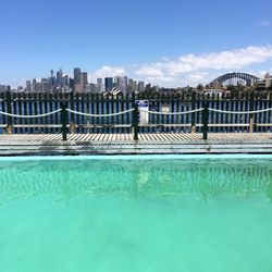Swimming pool and fence by sea against cityscape