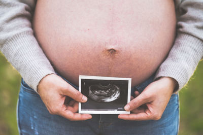 Midsection of pregnant woman holding ultrasound image