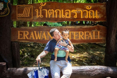 Father and daughter sitting against information sign