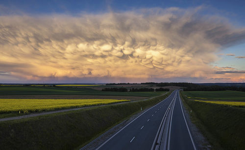 Road amidst field against sky during sunset