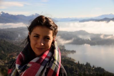 Portrait of smiling young woman wearing scarf while standing on mountain against sky