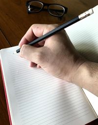 Cropped hand writing on book at table