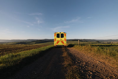 Ambulance car of emergency medical service leaving on rural dirt road in the middle of fields. 