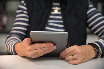 Midsection of woman using digital tablet at table