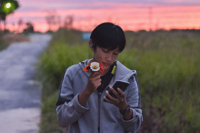 Someone holding a camera while standing in the field against the sky at sunset