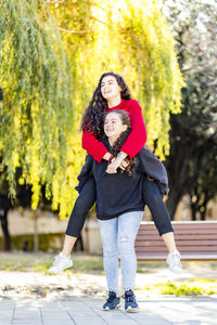 Happy teenage girl giving piggyback ride to friend in park