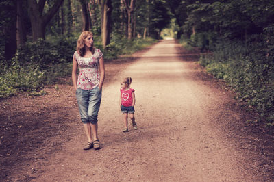 Front view of mother and daughter walking on pathway in forest