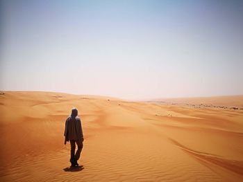 Full length rear view of man walking in desert against clear sky