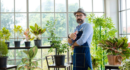 Portrait of young man standing against potted plants