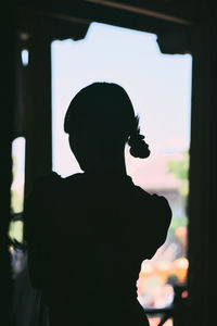 Silhouette woman standing by window