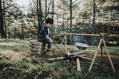 Boy preparing food while sitting on wood