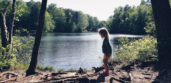 Rear view of woman standing by lake against trees