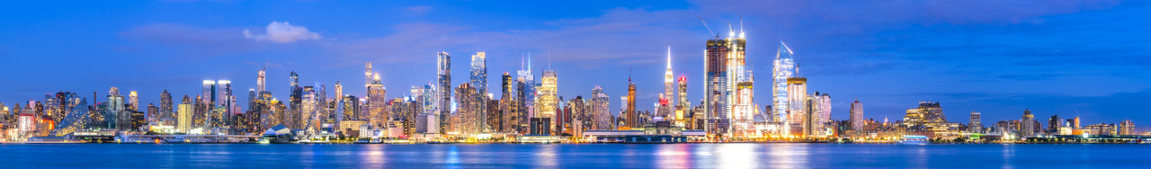 Panoramic view of illuminated buildings by sea against sky