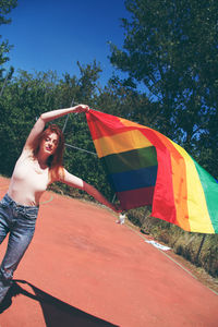 Portrait of young woman holding rainbow flag on sunny day