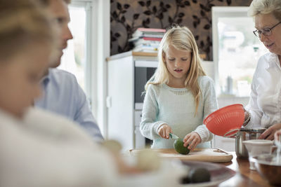 Girl cutting vegetables while cooking food with family in kitchen