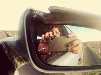 Reflection of young woman photographing car on side-view mirror