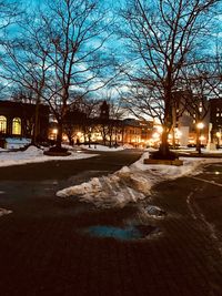 Snow covered road by bare trees in city at night