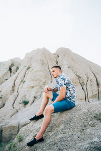 Young man sitting on rock against mountain
