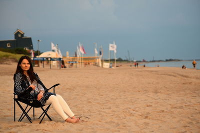 Woman sitting on chair at beach against sky