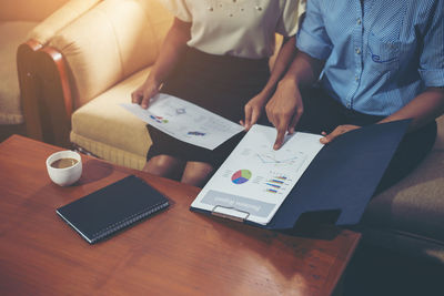 Midsection of business people holding graph chart while sitting on sofa in office