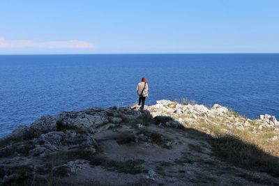 Man standing on rock by sea against sky