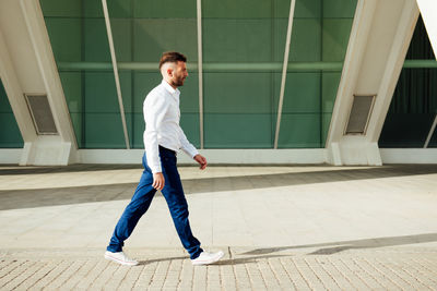 Side view of young man walking on floor against building