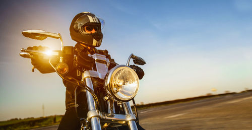 Low angle view of man riding motorcycle on road against sky during sunset