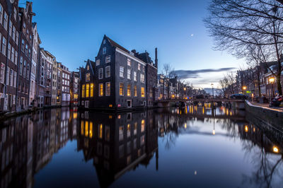 Illuminated buildings by river against sky in city at dusk