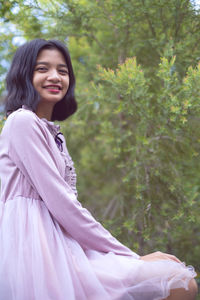 Portrait of smiling girl sitting against tree outdoors