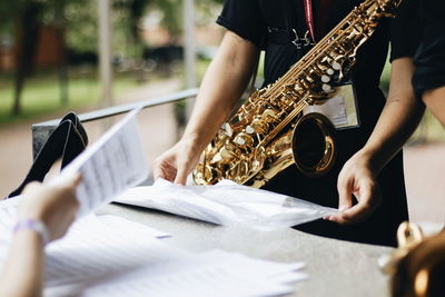Midsection of man with saxophone holding paper while standing by table