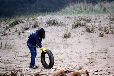 Woman rolling tire on sandy beach