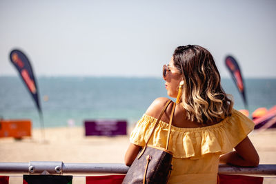 Rear view of woman standing by railing against beach