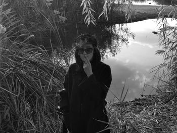 Young man wearing sunglasses smoking cigarette while standing by pond