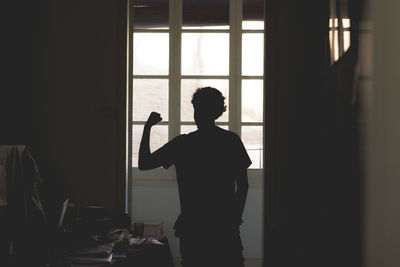 Rear view of silhouette man holding window at home