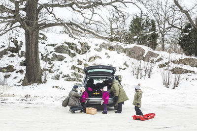 People sitting on snow covered trees during winter