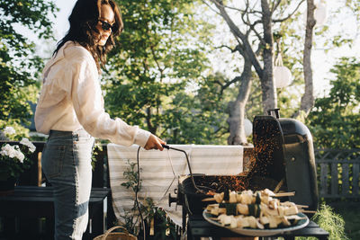 Woman grilling food on barbecue at yard during summer