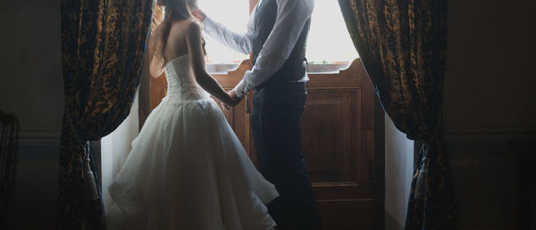 Low section of bride and groom standing by closed door at home